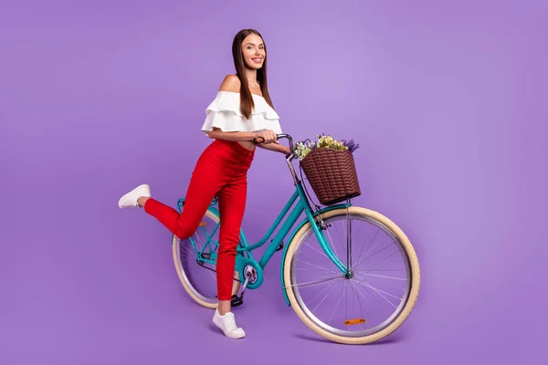 Foto van zorgeloze droom dame rijden fiets stand tiptoe dragen witte blouse broek sneakers geïsoleerde violette kleur achtergrond — Stockfoto