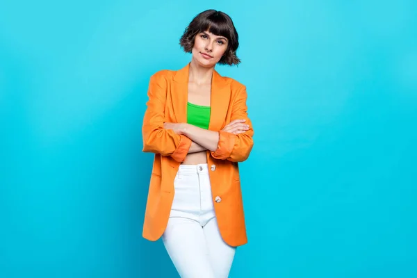 Foto van mooie jonge brunette dame gekruiste armen dragen oranje blazer top geïsoleerd op teal kleur achtergrond — Stockfoto