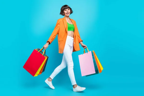 Plná délka fotografie šťastná žena držet ruce nákupní tašky chůze úsměv izolované na pastelové modré barvy pozadí — Stock fotografie