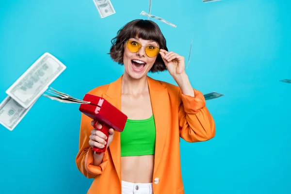 Photo of joyful young happy woman amazed hold money gun fall air blow cool isolated on blue color background — Stock Photo, Image