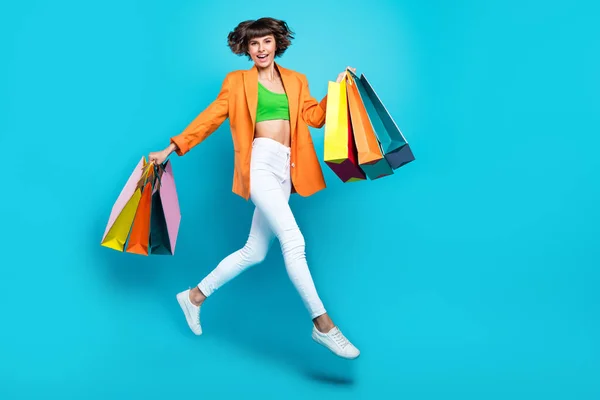 フルサイズの写真の若い幸せな正の女性ジャンプアップホールドショッピングバッグ販売ニュース孤立した上青色背景 — ストック写真