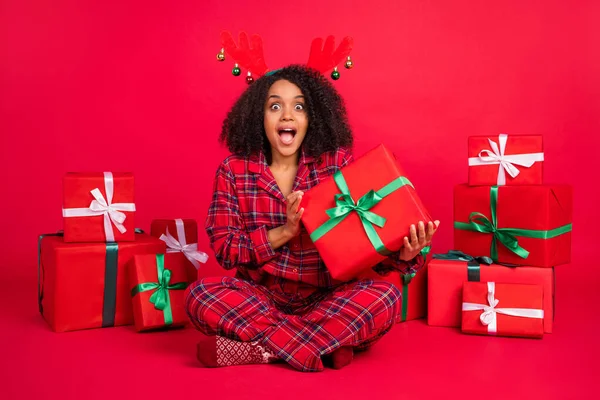 Πλήρης φωτογραφία μεγέθους του trendy κομψό μοντέλο afro αμερικανική κυρία φορούν hleepwear κεφαλόδεσμο Χριστούγεννα κρατήσει δώρο κατάπληκτος απομονώνονται σε φόντο κόκκινο χρώμα — Φωτογραφία Αρχείου