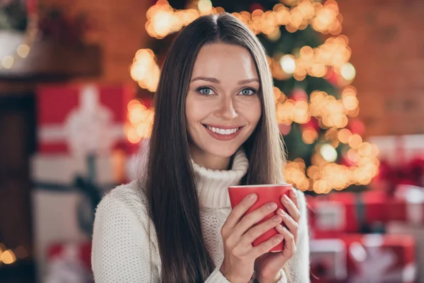 Çekici bir genç bayanın fotoğrafı beyaz kazak giyip gülümsüyor ve evin içinde lezzetli bir kahve içiyor. — Stok fotoğraf