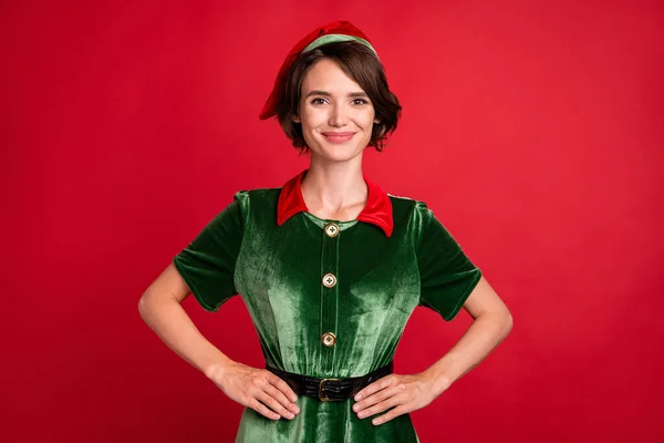 Foto de confiante positivo adorável senhora mãos quadris olhar câmera desgaste elfo traje chapéu isolado cor vermelha fundo — Fotografia de Stock
