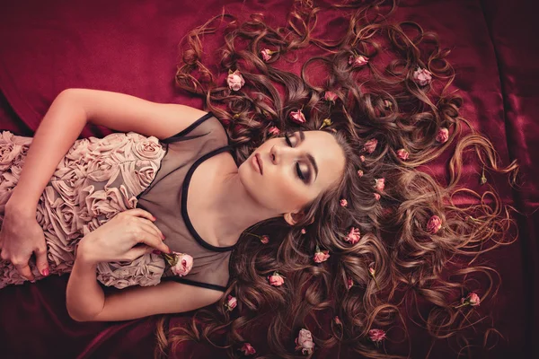Haare mit Rosen dehnen sich auf dem textilfarbenen Marsala aus. Ansicht von oben Bild eines Mädchens mit langen lockigen Haaren. — Stockfoto