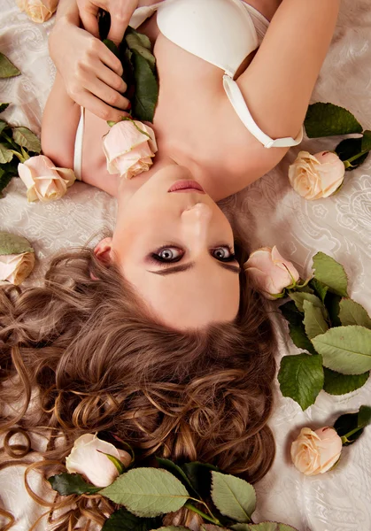 Rapariga com rosas. imagem vista superior de uma menina que está deitada em lingerie na cama com rosas — Fotografia de Stock