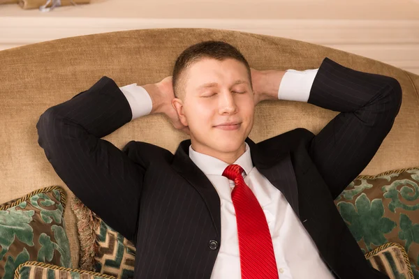 Successful handsome man sitting on the couch after work. young businessman put his hands behind his head, resting and smiling — Stock Photo, Image