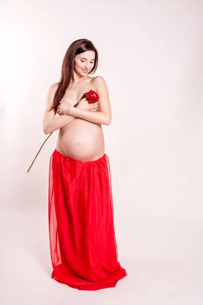 Красивая беременная девушка обнимает свой голый животик. красивая девушка в красной юбке и красный бюстгальтер стоя на белом фоне — стоковое фото