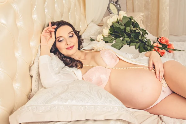 Pregnant in beautiful underwear lying on the luxurious white bed and stroking her tummy — Stock Photo, Image