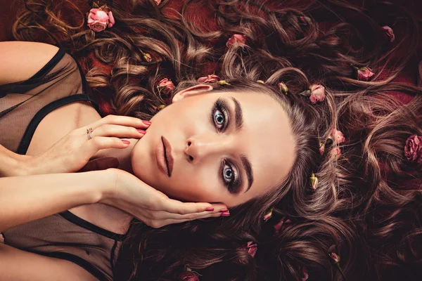 Hair with roses expand on the fabric colored Marsala. top view image of a girl with long curly hair.
