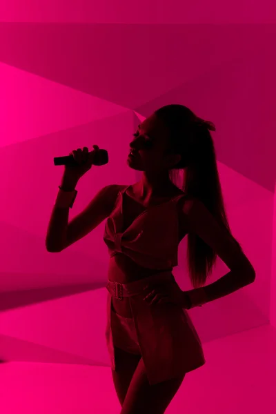 A silhueta da rapariga. menina esbelta cantando com um microfone — Fotografia de Stock