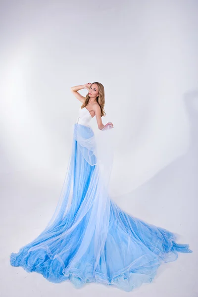 Hermosa chica en un vestido largo azul con pluma en un fondo blanco — Foto de Stock