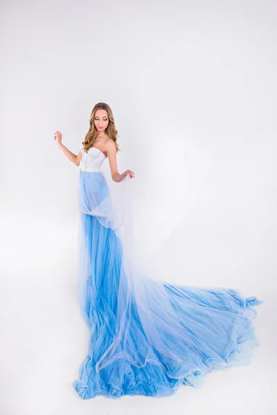 Hermosa chica en un vestido largo azul con pluma en un fondo blanco — Foto de Stock