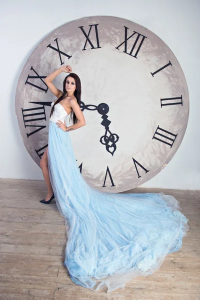 Lány egy hosszú ruha plume áll közel a hatalmas óra — Stock Fotó