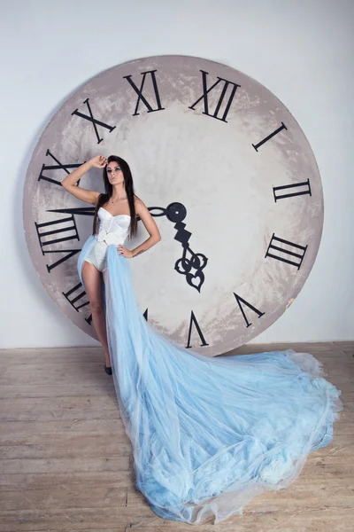 Menina em um vestido longo com pluma de pé perto do relógio enorme — Fotografia de Stock