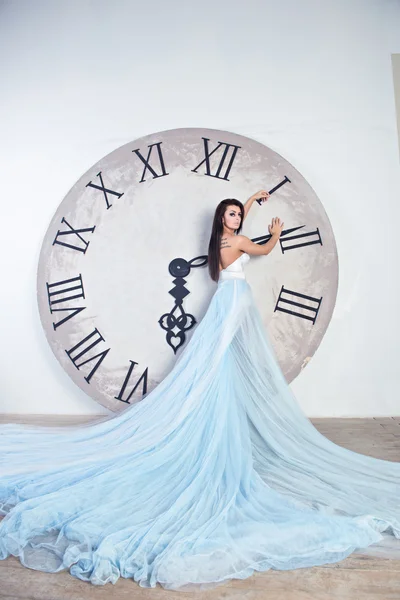 Menina em um vestido longo com pluma de pé perto do relógio enorme — Fotografia de Stock