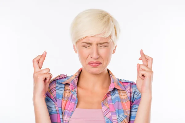 Waiting for special moment. Portrait of young woman in shirt keeping fingers crossed and eyes closed while standing against white background — Stock Fotó