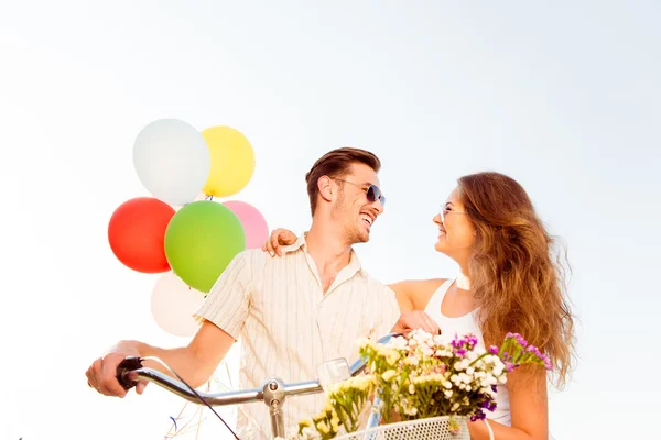 Pareja enamorada en bicicleta con globos y flores —  Fotos de Stock