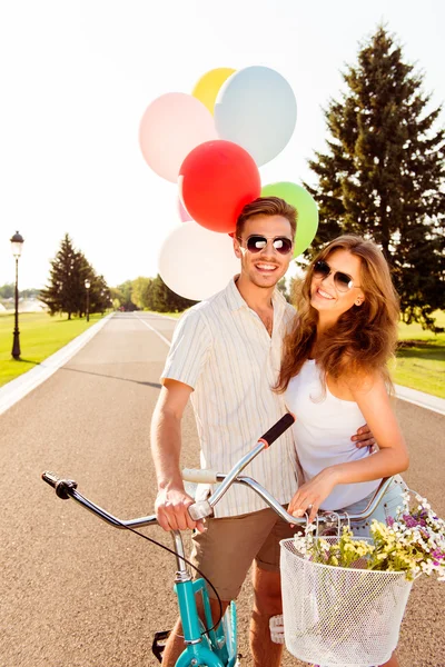 Casal apaixonado em bicicletas com balões e flores — Fotografia de Stock