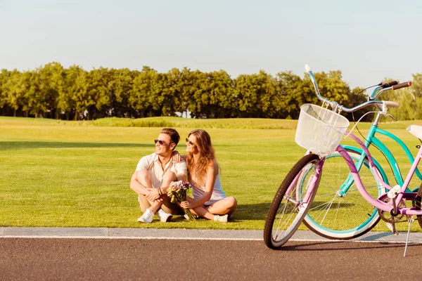 Pareja joven sentada en el césped cerca de sus bicicletas — Foto de Stock