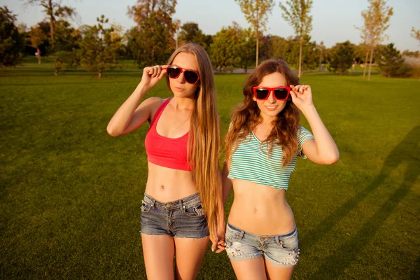 Two young slim girls holding hands and glasses in the park — Stock Photo, Image