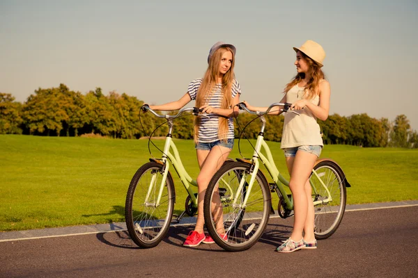 Duas garotas bem torneadas juntas andando com uma bicicleta — Fotografia de Stock