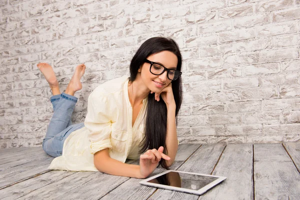 Mignonne femme intelligente avec des lunettes couché sur un sol en bois avec une languette — Photo