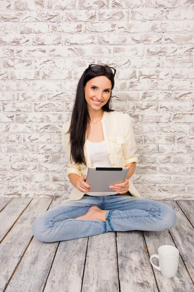 Mignonne fille assise sur un sol en bois avec une tablette et une tasse de c — Photo