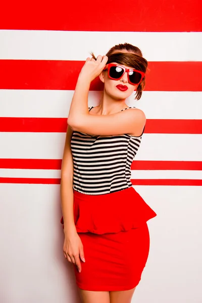 Aranyos lány piros ajkak és a szemüveg a csíkos b elleni pózol — Stock Fotó
