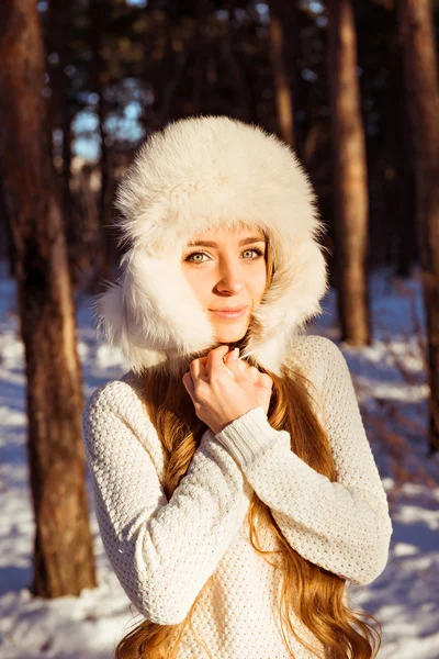 Schönes Mädchen mit weißer Pelzmütze im Winterwald — Stockfoto