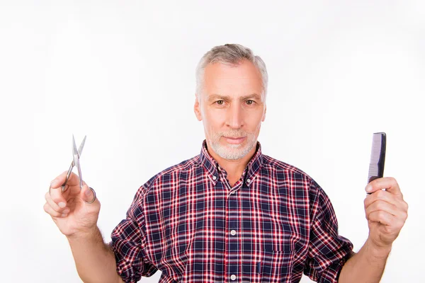 Confident aged man choosing between scissors and comb — Stock Photo, Image