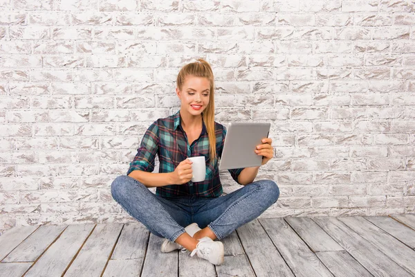 Joyeux fille mignonne avec tablette et tasse assis sur le plancher — Photo