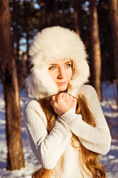 Happy cute girl wearing white fur hat in winter forest — Stock Photo, Image