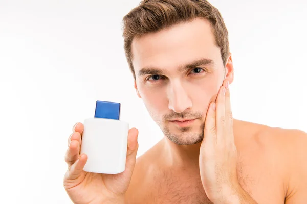 Handsome young man holding lotion after shave touching face — Stock Photo, Image