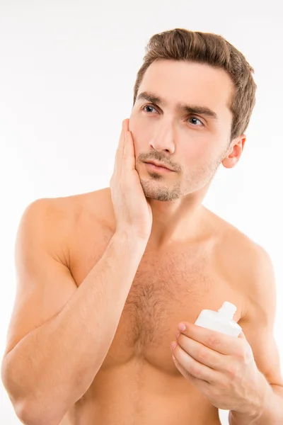 Handsome young man holding lotion after shave smearing cheek — Stock Photo, Image