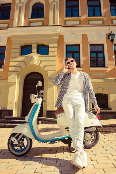 Ung vacker man står nära en motorcykel talar på phonen — Stockfoto