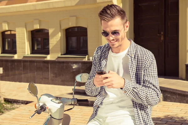 英俊的快乐男人，坐在摩托车上键入一条消息 — 图库照片