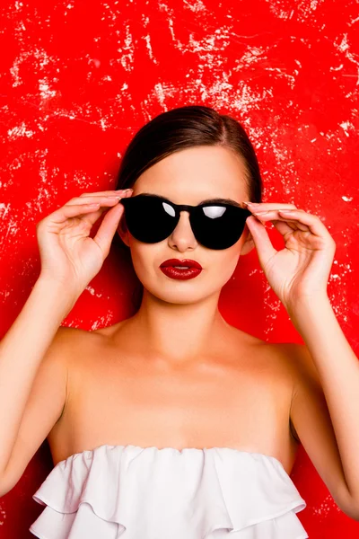 Divatos csinos lány tartja a szemüveg, szemben a vörös háttérben — Stock Fotó