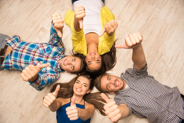 Fröhliche junge Leute, die auf dem Boden liegen und Daumen nach oben zeigen — Stockfoto