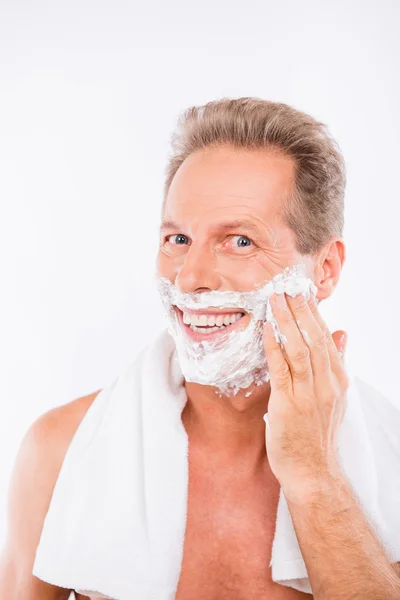 Guapo hombre feliz con toalla untando espuma de afeitar en su barbilla —  Fotos de Stock