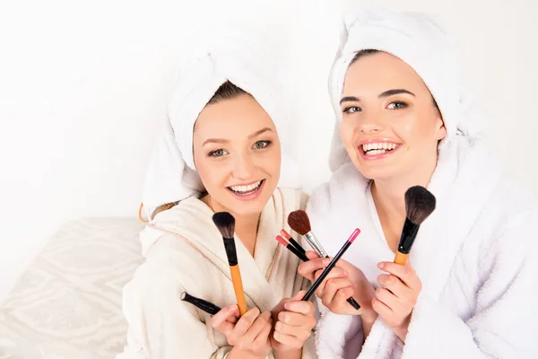 Mooie jonge vrouwen houden make up borstels met handdoeken op hun hea — Stockfoto