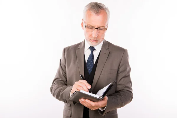 Homem de negócios envelhecido em um terno elegante com óculos escrevendo notas — Fotografia de Stock