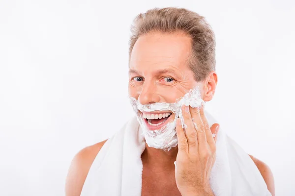 Handsome happy man with towel smearing shaving foam on his chin — Stock Photo, Image