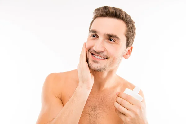 Handsome man holding lotion after shave smearing cheek — Stock Photo, Image
