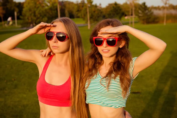 Two young slender girls with glasses watching sunset in the park — Stock Photo, Image