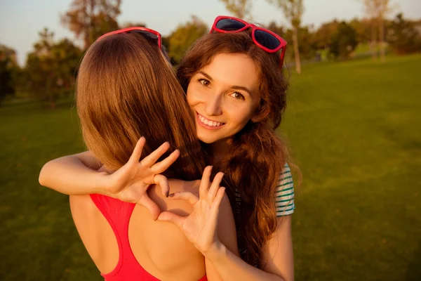 Dos chicas jóvenes y encantadoras abrazándose y mostrando el corazón — Foto de Stock