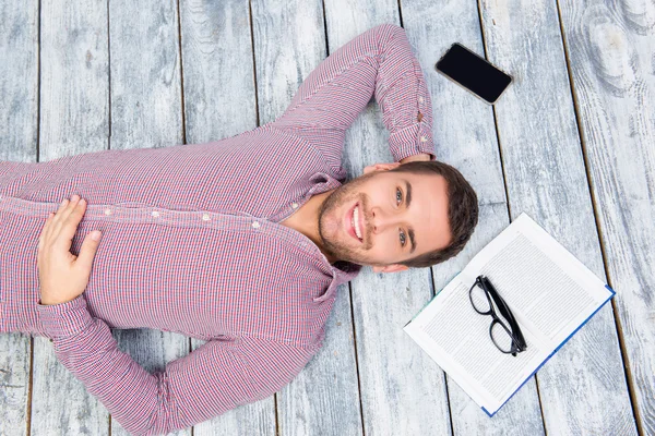 Vista superior de la foto del hombre sonriente acostado en el suelo con libro, pho — Foto de Stock