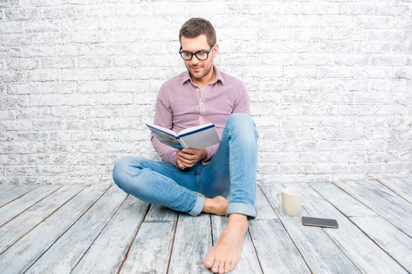 Jonge man in glazen zittend op de vloer en het boek lezen — Stockfoto