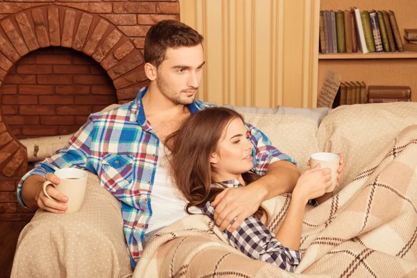 Щаслива пара закохана в плетених і чашок, що сидять на дивані — стокове фото