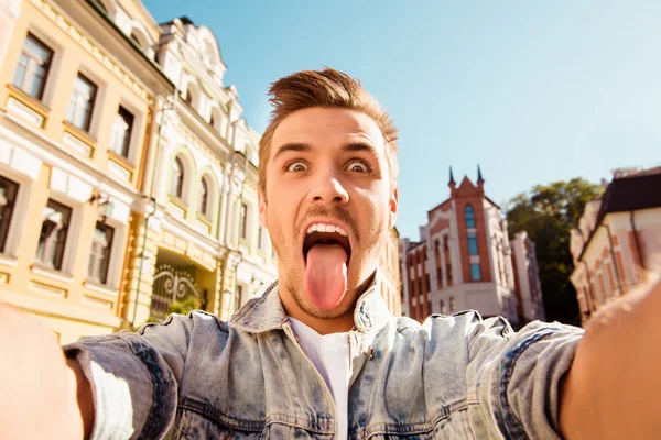 Funny happy man making comic selfie with tongue on the street — Stock Photo, Image